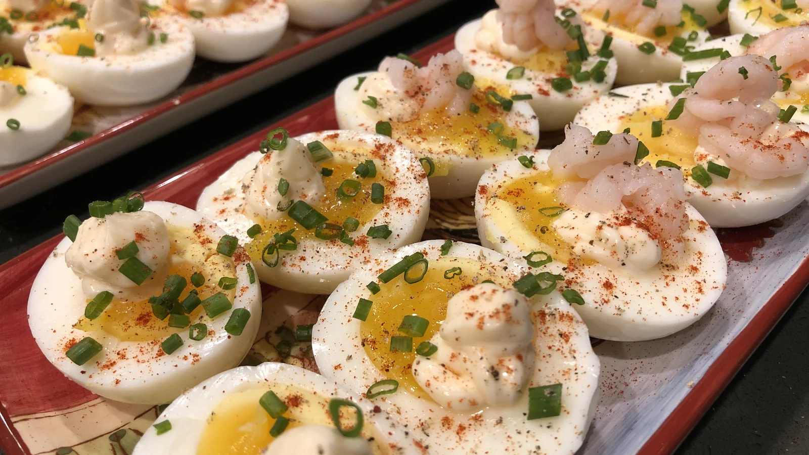 Soft-boiled egg halves on platters with chives, paprika, and shrimp.