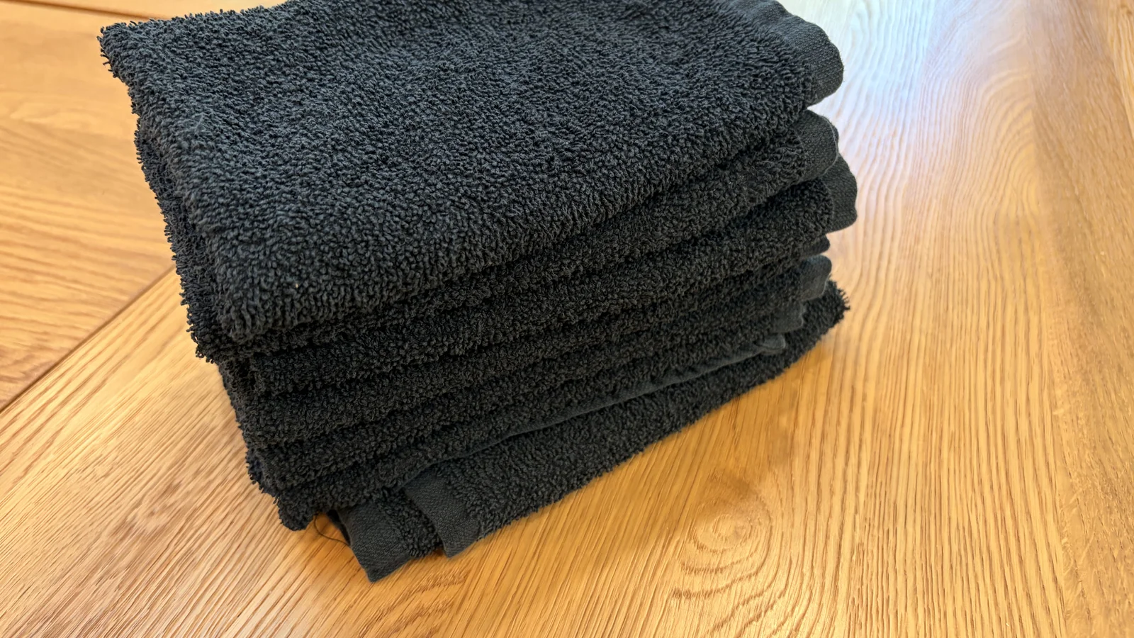 Stack of folded black terry bar towels on a light wood surface