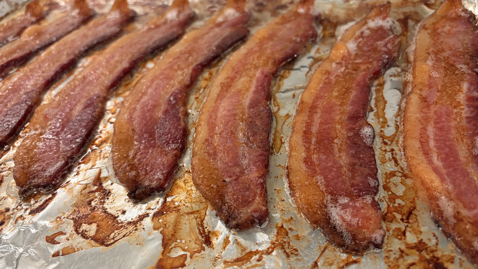 Thick bacon strips cooked on a foil-lined baking sheet.