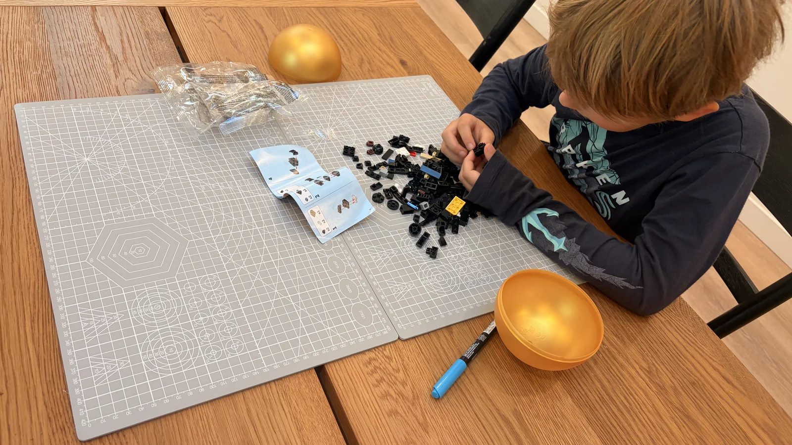 Child building Lego on a grey craft mat spread across a light wood dining table