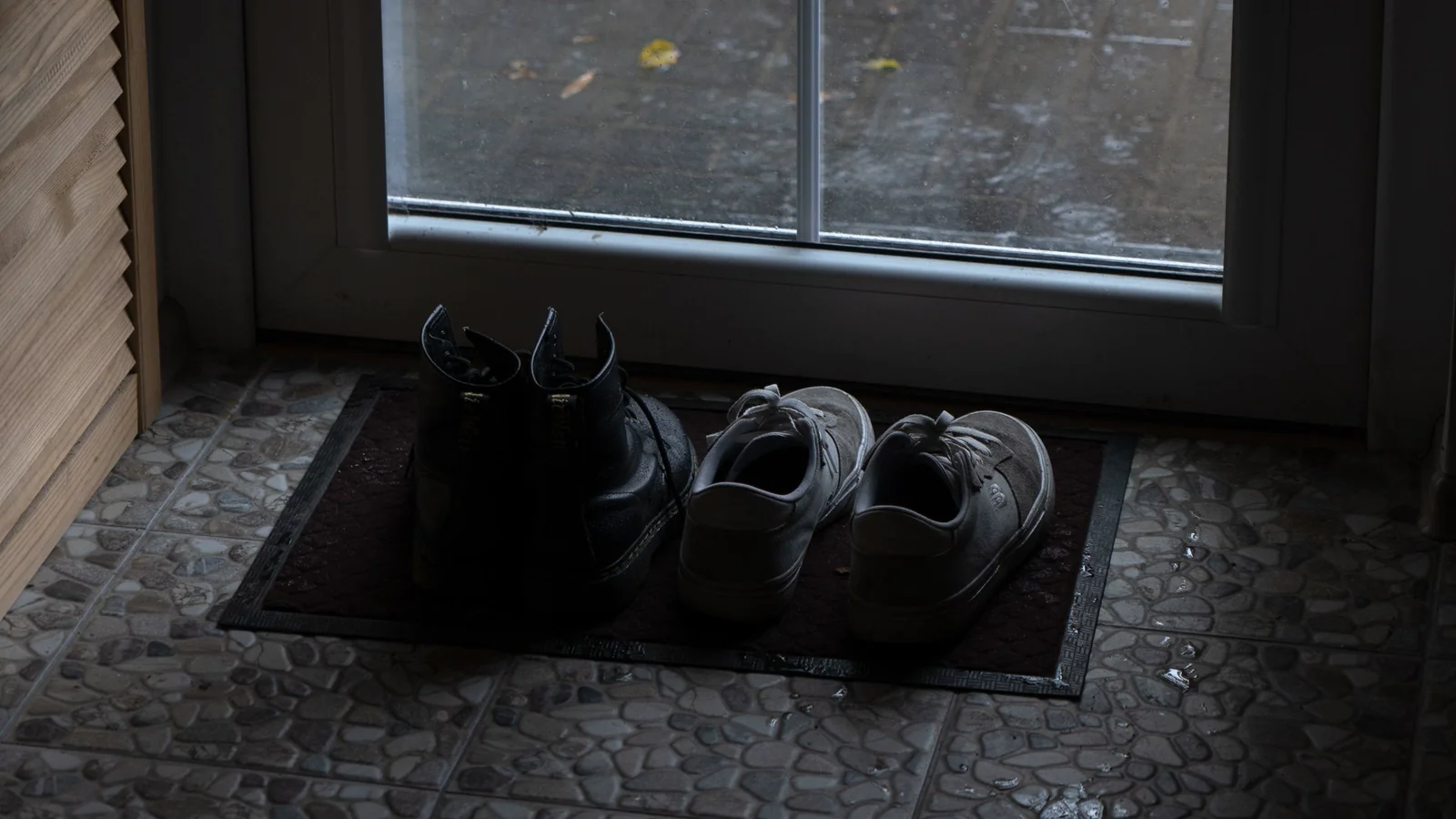 Two pairs of shoes on a doormat by the front door on a rainy morning.
