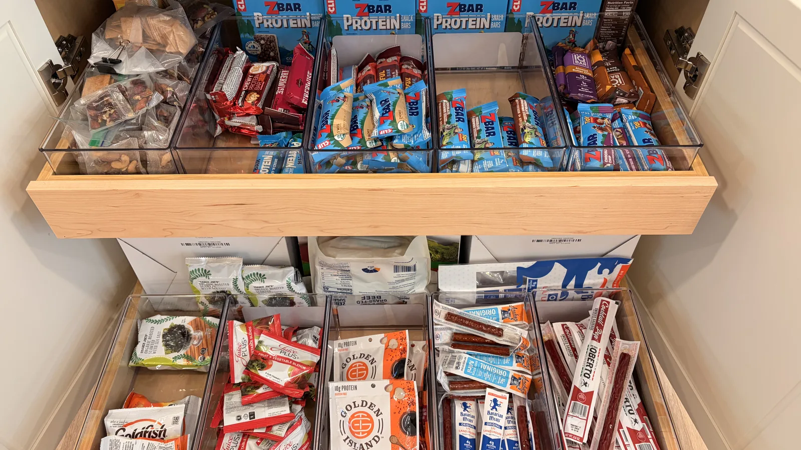 Pull-out kitchen drawers with clear bins of bars, seaweed snacks, jerky, and meat sticks the kids can reach.
