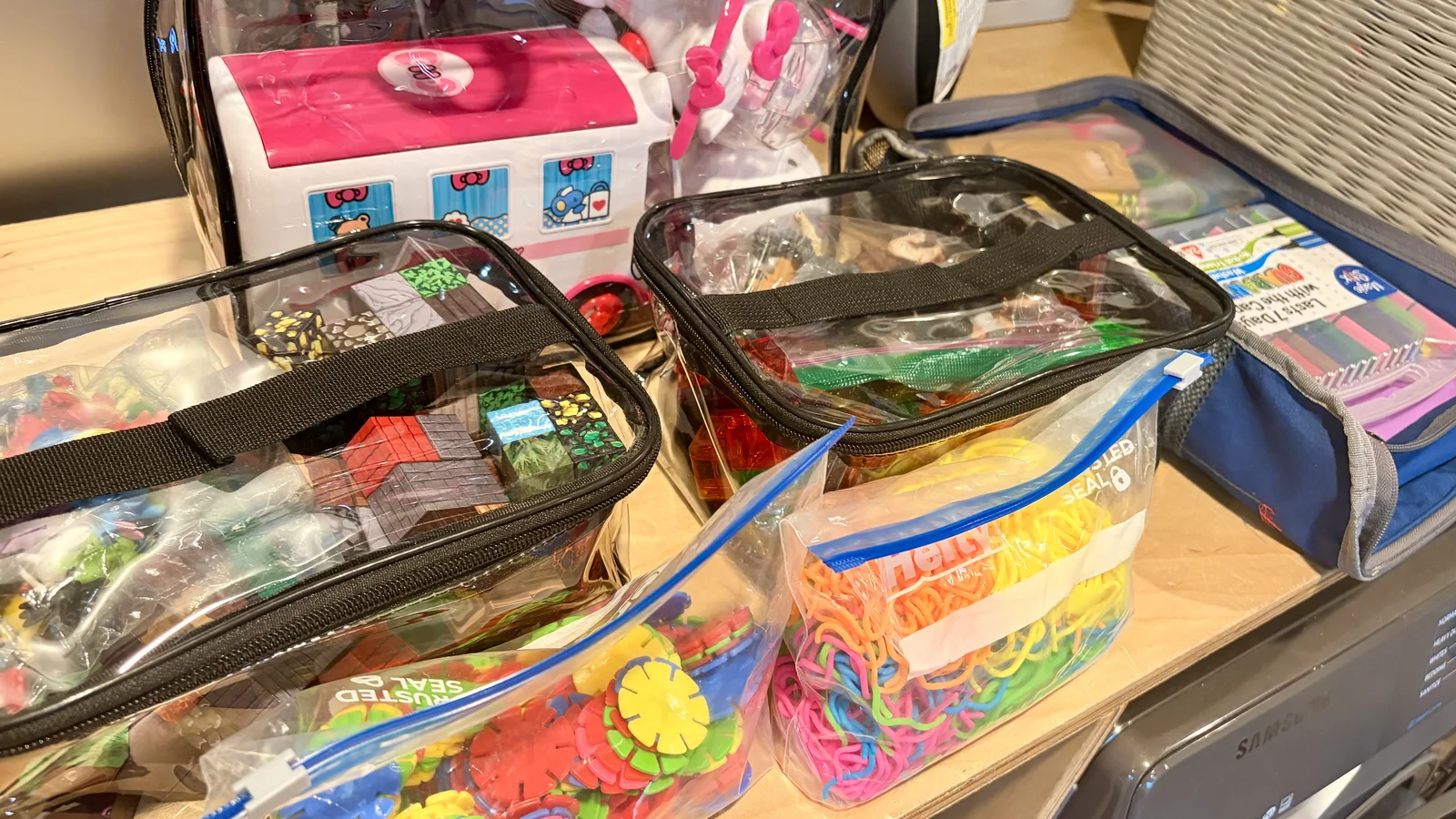 Clear travel bags packed with Magna-Tiles, Minecraft magnetic cubes, figurines, and travel art supplies on a wood surface