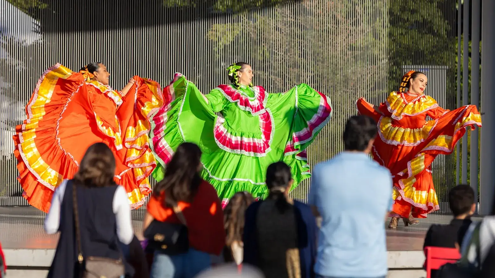 Dancers in black and red dresses performing on a paved plaza, with an audience and a red canopy tent.